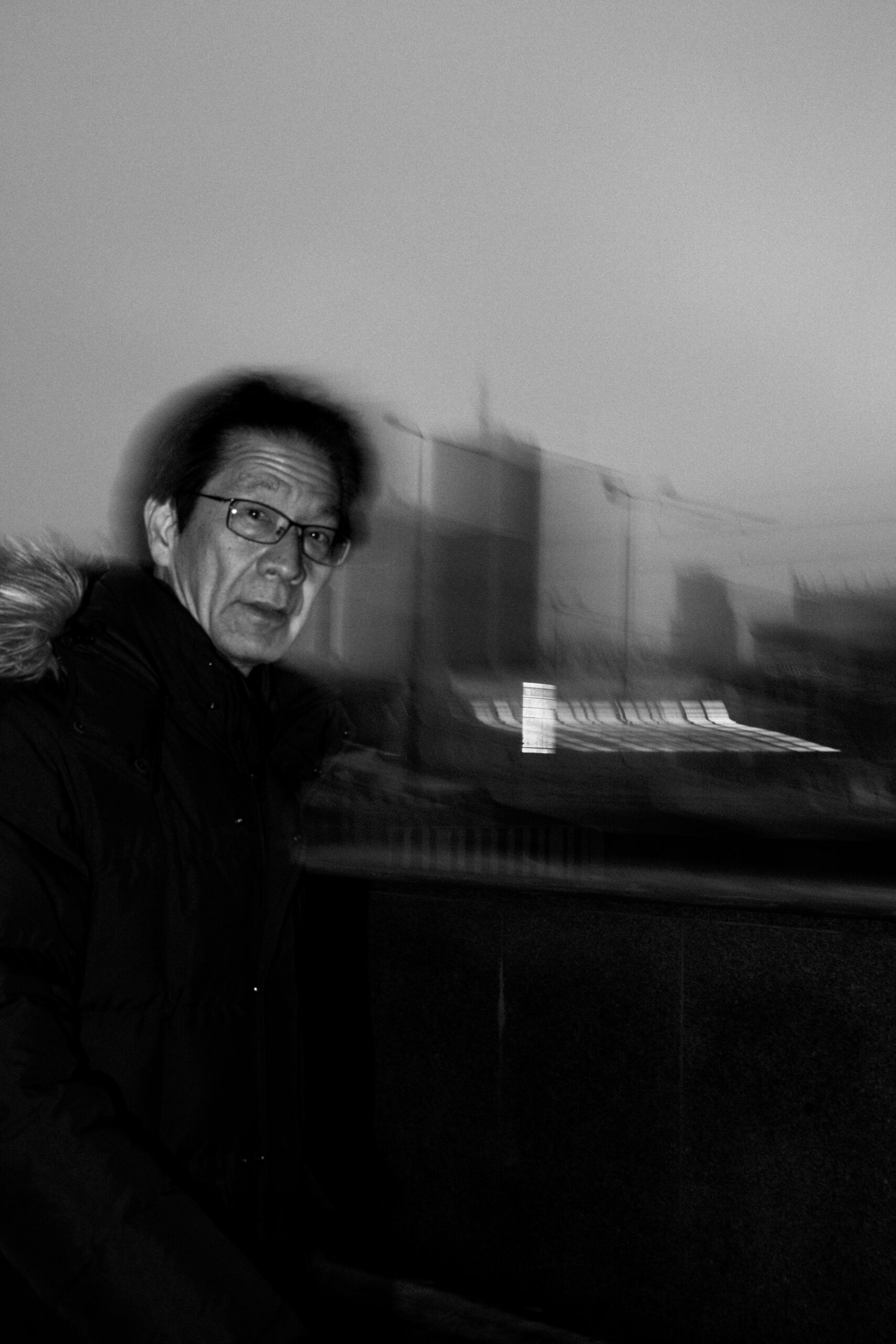 A man in glasses against a motion-blurred city skyline at dusk