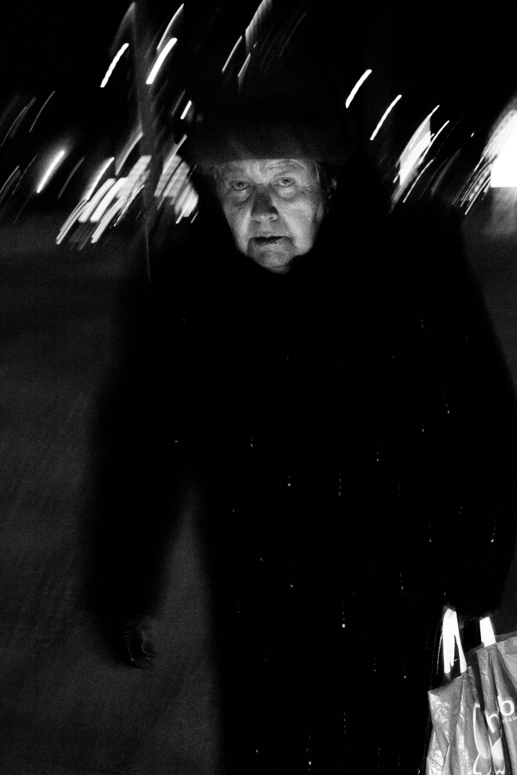 An elderly woman in a dark coat staring into the lens among streaks of light