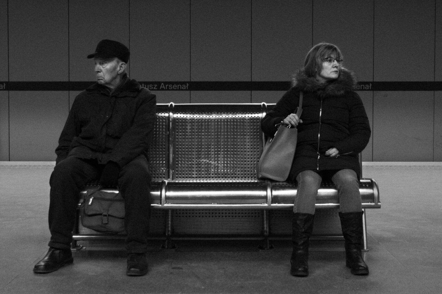 A man and a woman looking away from each other on a platform bench at Ratusz Arsenał