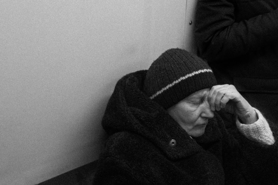 An elderly woman in a knitted hat resting her head on her hand, eyes closed